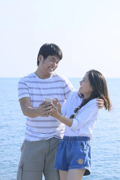 Young man and woman with mobile phone in hand  standing at sea s — Stock Photo, Image