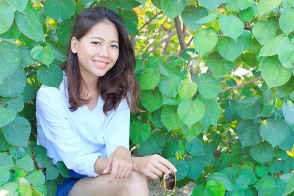 Retrato de una mujer bonita sentada en hojas verdes arbusto y sonriente —  Fotos de Stock