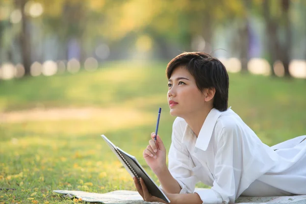 Mujer joven acostada en el parque de hierba verde con lápiz y cuaderno — Foto de Stock