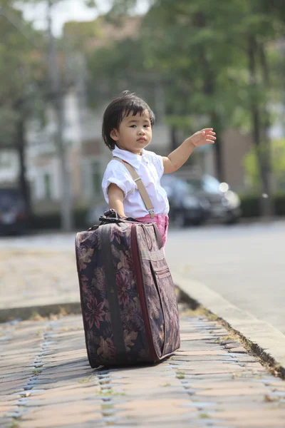 Young children standing with big suitcase beside traffic street — Stock Photo, Image