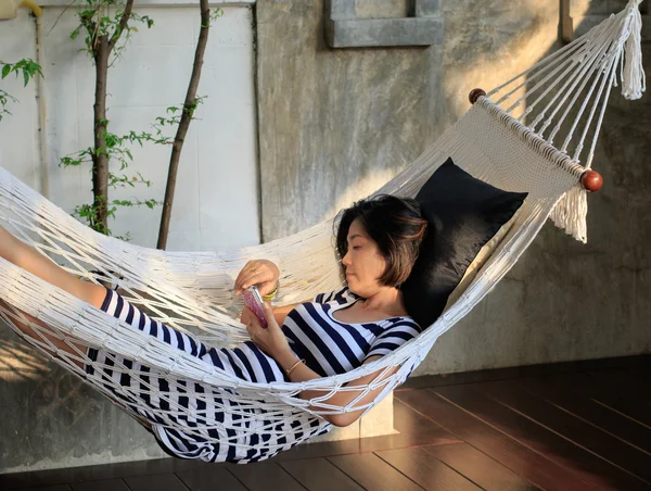 Woman lying on cradle looking on smart phone in hadn with relaxing emotion — Stock Photo, Image