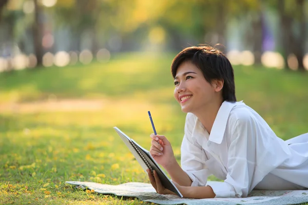 Mujer joven acostada en el parque de hierba verde con lápiz y cuaderno — Foto de Stock