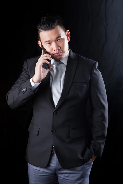 Young asian business man talking on mobile phone against black b — Stock Photo, Image