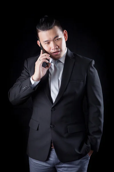 Portrait of asian business man talking mobile phone against blac — Stock Photo, Image