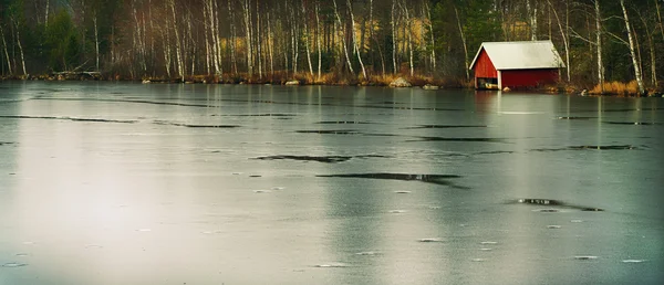 Frusen sjö med liten stuga och skog — Stockfoto