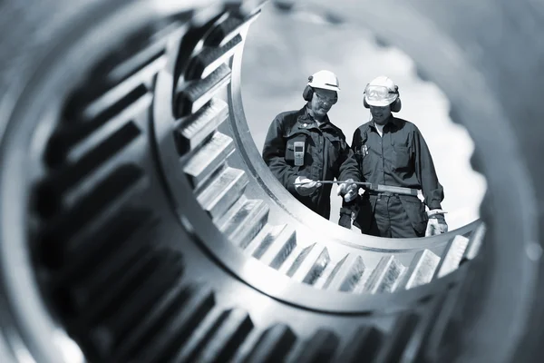 Metal workers seen through giant gears — Stock Photo, Image