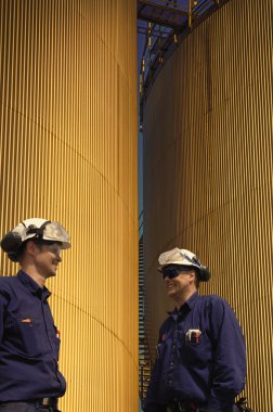 rafineri işçileri ve gün batımında büyük yakıt depolama tankları