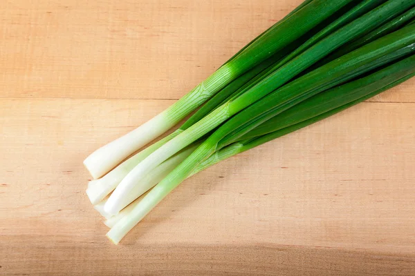 Cebollas verdes frescas en una tabla de madera — Foto de Stock