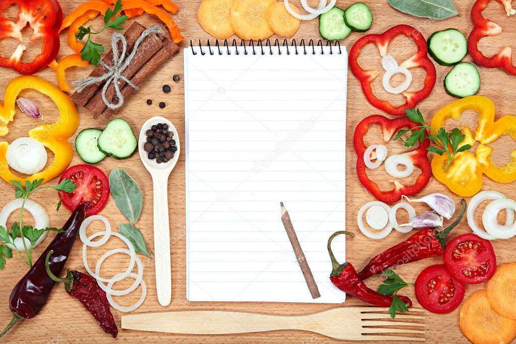 Vegetables, spices and notepad for recipes, on wooden table.