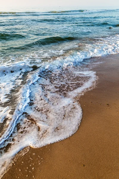 Zee golven in het witte schuim op het zandstrand. Dawn. — Stockfoto