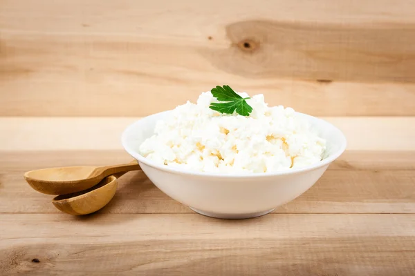 Queso cottage fresco en un tazón blanco sobre una mesa de madera . —  Fotos de Stock