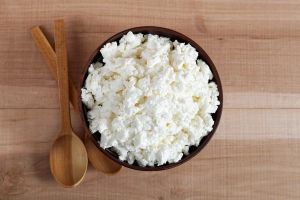 Fresh cottage cheese in a bowl with spoon on a wooden table.