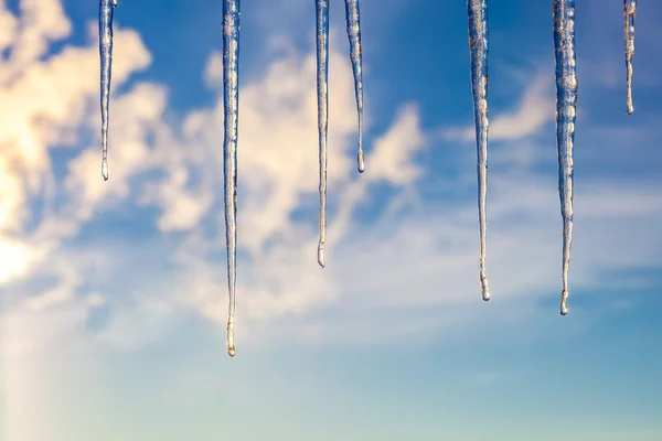 Istappar mot en blå himmel med moln — Stockfoto