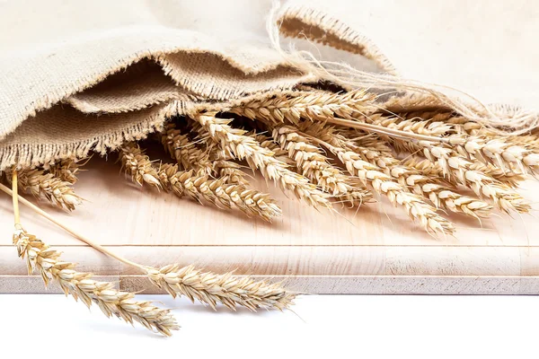 Sheaf of wheat ears in a cloth on a wooden board. — Stock Photo, Image