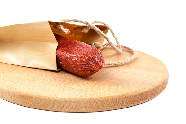 Stick sausage in a paper bag on a wooden cutting board. — Stock Photo, Image