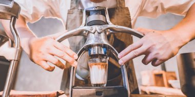 Profesyonel barista sıcak içecek espresso yapıyor. Eskimiş ahşap masa üzerinde kahve yapıyor. Kafede yavaş bir bar, sabahları cam bir fincana kafein hazırlıyor.