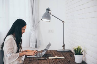 Asyalı bir kız evde dizüstü bilgisayarla çalışıyor. Evde oturuyor, arıyor ve not yazıyor. 