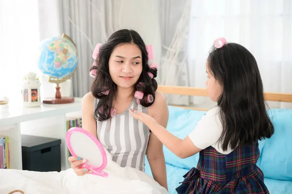 happy family, play time, daughter doing hair style for mom, mother and kid playing together on the bed, family concept, asian girl, school uniform, black hair, roll hair in the bedroom, daytime.