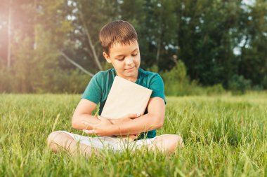 Çimenlerin üzerinde bir kitapla genç çocuk