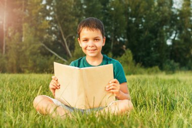 Çimenlerin üzerinde bir kitapla genç çocuk