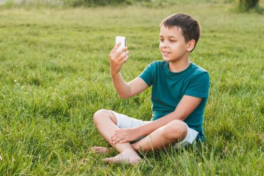 Çimlerin üstünde a telefon ile genç çocuk