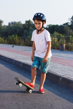 Çocuk bir kaykay ile açık havada duruyor