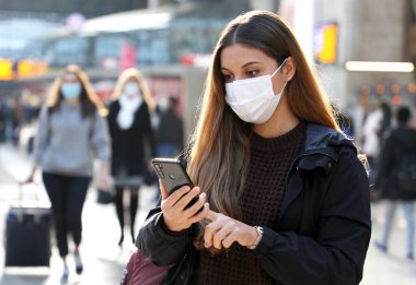 Havaalanında veya istasyonda Coronavirus 'u önlemek için cep telefonu takarak yürüyen üniversite öğrencisi.