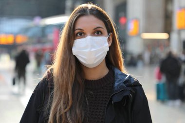 Tren istasyonunda cerrahi maske takan genç bir kadının portresi.