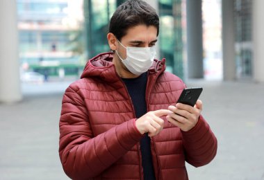Modern şehirde akıllı telefon uygulaması kullanarak cerrahi maske takan bir adam.
