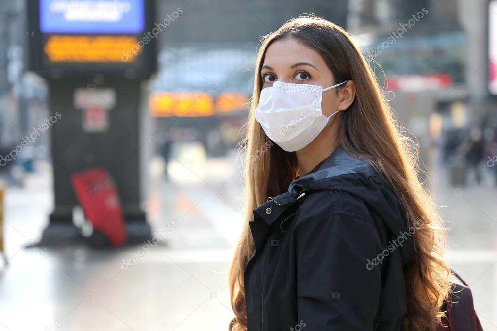 Portrait of traveler woman wearing surgical mask at train station looking worried in front of her. Copy space.