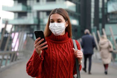 Şehir caddesinde ameliyat maskesi takıp cep telefonuyla sohbet eden genç bir iş kadını. Dışarıda akıllı telefon kullanan koruyucu maskeli bir ofis çalışanı..