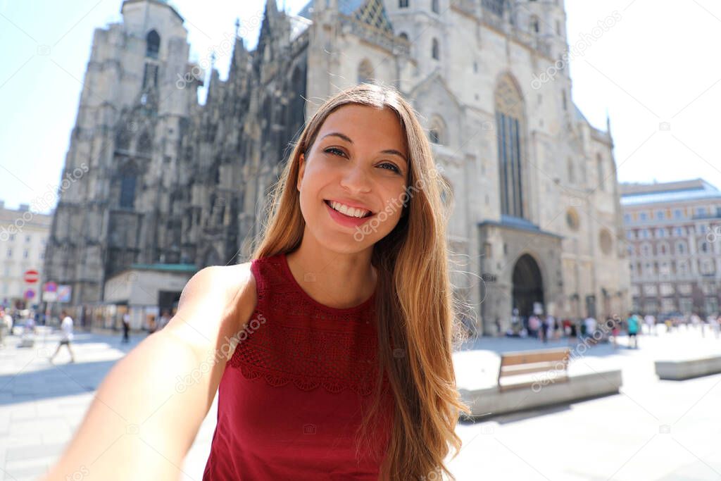 Beautiful smiling tourist girl taking self portrait with smartphone in Vienna with Saint Stephen's cathedral on the background in Austria, Europe