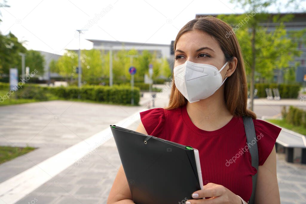 Portrait of beautiful girl with FFP2 KN95 face mask holding folders looking to the side outdoors