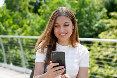 Dışarıda cep telefonundan mesaj gönderen mutlu, güzel bir genç kadın.