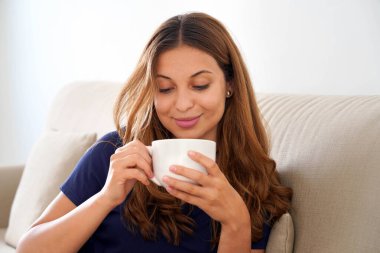 Beautiful woman dreaming sitting on comfortable sofa tasting herbal tea