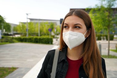 Beautiful young woman with FFP2 KN95 medical mask looking worried to the side in the street