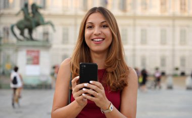 Şehir tarihinin arka planına gülen çekici genç bir kadın. Genç bir kadın, sıradan bir şekilde kameraya bakıp gülümsüyor..