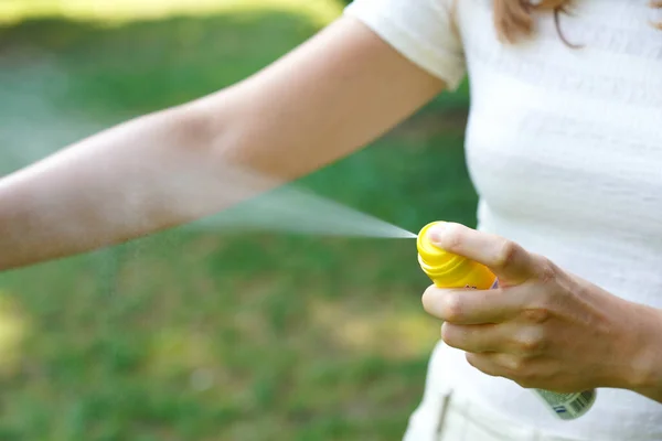 Young woman applying mosquito repellent on her arm during hike in nature. Insect repellent. Skin protection against tick and other insect. Focus on the top of spray container.