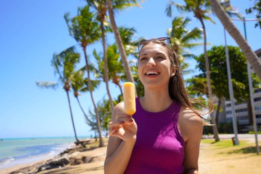 Sahilde buzlu dondurma yiyen İspanyol bir kadın. Arka planda palmiye ağaçları var. Yaz tatili kavramı.