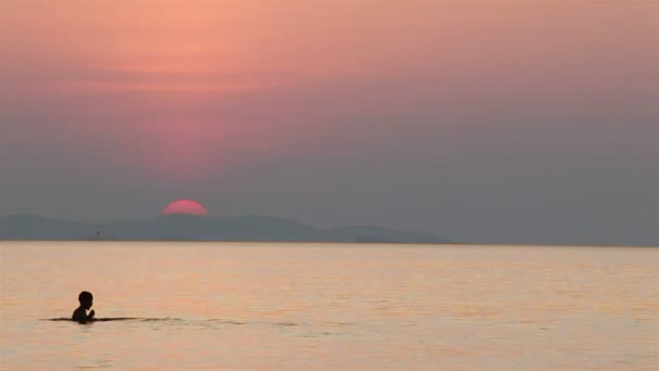 Solnedgången i havet och siluetten av barn simning — Stockvideo