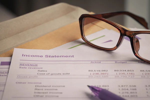 Surat pernyataan pendapatan pada amplop coklat dan kacamata, pena, bu — Stok Foto