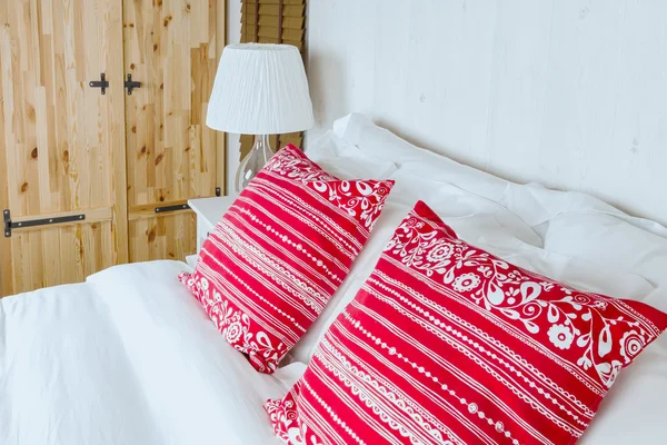 Red pillow on bedroom with white bed sheet and lamp — Stock Photo, Image