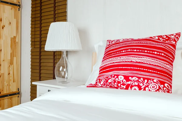 Oreiller rouge sur chambre avec drap de lit blanc et lampe — Photo
