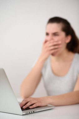 Bilgisayardaki kız esniyor. Ağzını elinle kapat. Odaklan. dizüstü bilgisayar ön planda.