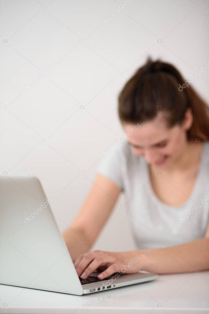The girl is out of focus sitting at the computer and laughing. Head tilted downwards. Bloger