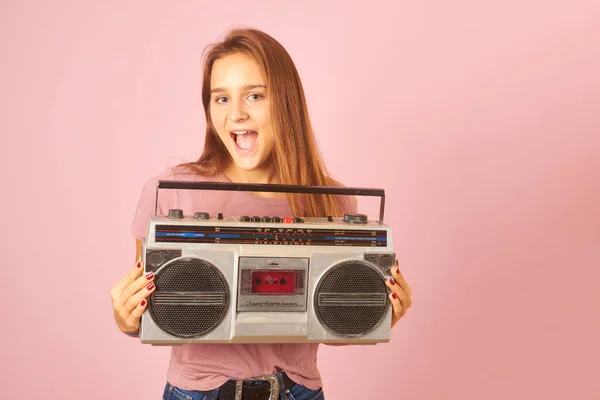 用粉色背景的老式收音机盒式磁带听音乐的年轻妇女 — 图库照片