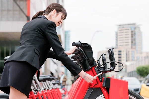 Bizneswoman wynajem wspólnego roweru elektrycznego na ulicy miejskiej w drodze do pracy — Zdjęcie stockowe