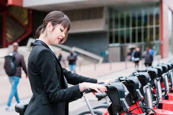 Üzletasszony bérel egy közös elektromos kerékpár a város utcájában munkába menet Stock Kép