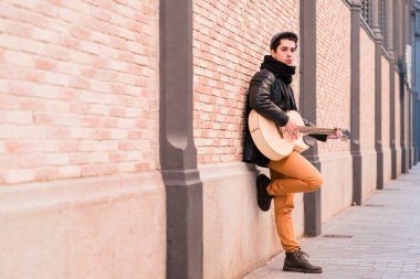 Sokak müzisyeni akustik gitar çalıyor. Paltolu ve şapkalı genç bir delikanlı.