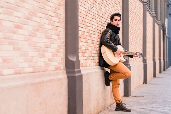 Músico de rua tocando guitarra acústica. Jovem homem de mão vestindo casaco e chapéu ao ar livre — Fotografia de Stock